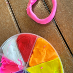 A circle of pink playdough (rolled into a snake and connected into a circle) beside a tray of multi-colored playdough.